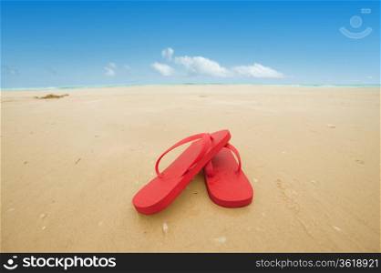 Red flip flops on the beach sand.Concept of summer vacations