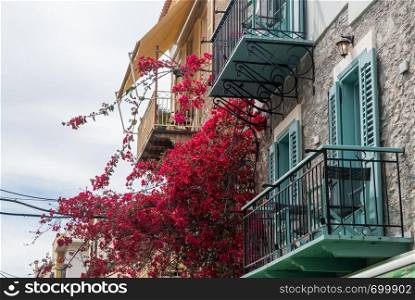 Red flowers on balconies above narrow streets in the old town in the city of Nafplio in Greece. Narrow streets in Old Town of Nafplio