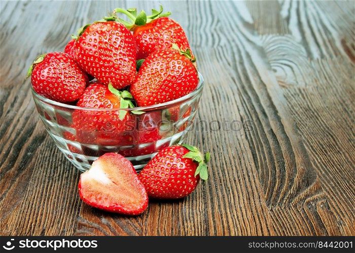 Red fresh strawberry in a transparent bowl on brown wooden background with copy space for text. Strawberry in a bowl on brown wooden background