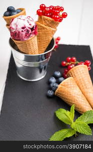 Red fruits ice cream cone on black slate board.