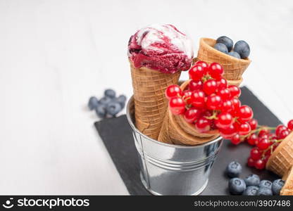 Red fruits ice cream cone on black slate board.