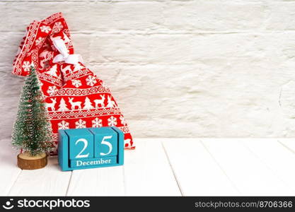 Red gift bag, decorative Christmas tree and blue wooden perpetual calendar of cubes on white brick wall background. Top view, flat lay with copy space, banner, header, New Year background