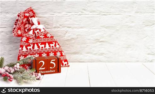 Red gift bag, decorative Christmas tree and red wooden perpetual calendar of cubes on white brick wall background. Top view, flat lay with copy space, banner, header, New Year background