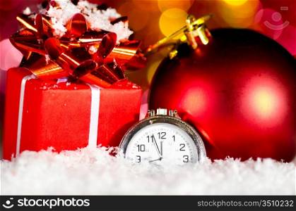 red gift box and ball on snow with clock on blurred background