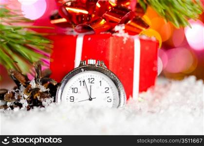 red gift box and clock on snow with christmas tree branch on blurred background