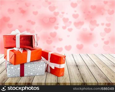 Red gift box and heart shape on wood table top with heart blur bokeh background, valentines day concept.