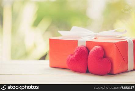Red gift box and heart shape on wood table top with nature green blur bokeh background, valentines day concept.