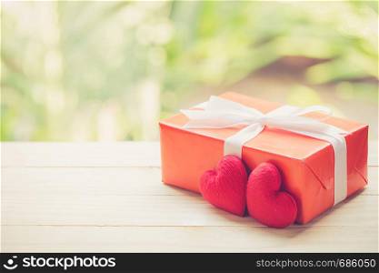 Red gift box and heart shape on wood table top with nature green blur bokeh background, valentines day concept.