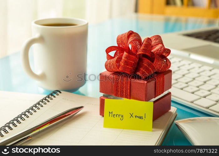 Red gift box and paper note with Merry xmas message on office table, concept to christmas greeting and holiday season