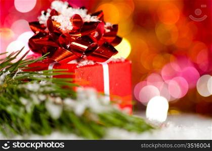 red gift box on snow with christmas tree branch on blurred background