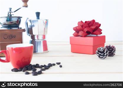 Red gift box with coffee pot, coffee grinder, red cup and roasted coffee beans on wooden table, Selective focus