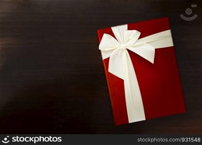 Red gift box with white bow on black table with free space for text.