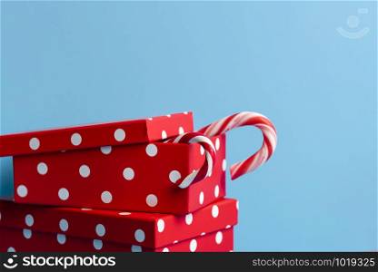 Red gift boxes with white spots and candy canes, on a blue background. Christmas presents. Xmas red gifts. Gifting concept. Winter holiday tradition.