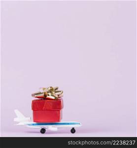 red giftbox with golden bow toy airplane against pink background