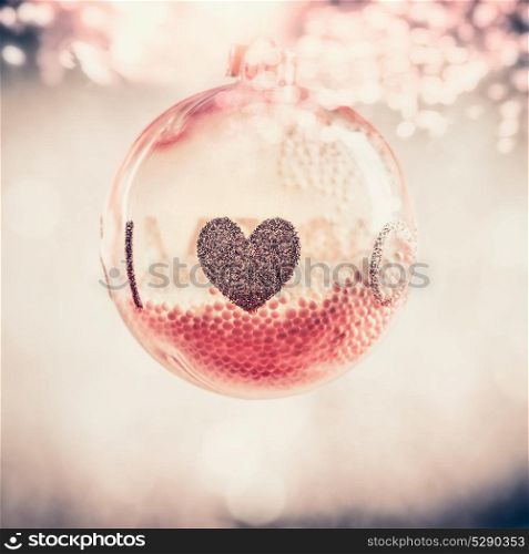 Red glass Christmas hanging ball with heart at bokeh background, festive greeting card