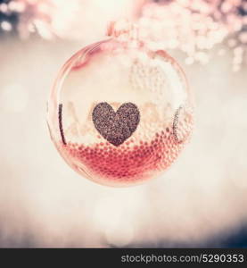 Red glass Christmas hanging ball with heart at bokeh background, festive greeting card