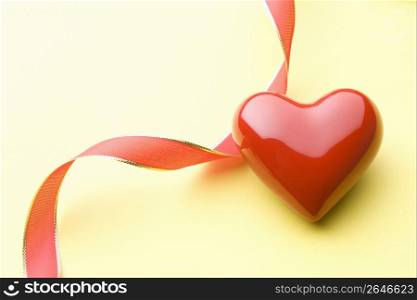 Red glass heart with red ribbon isolated on a yellow background