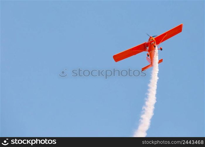 Red glider plane emits white smoke in a blue sky. Air show. Red glider plane emits white smoke in blue sky