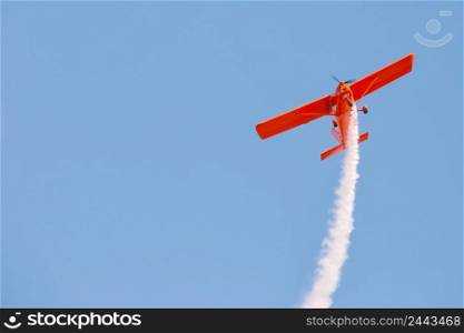 Red glider plane emits white smoke in a blue sky. Air show. Red glider plane emits white smoke in blue sky