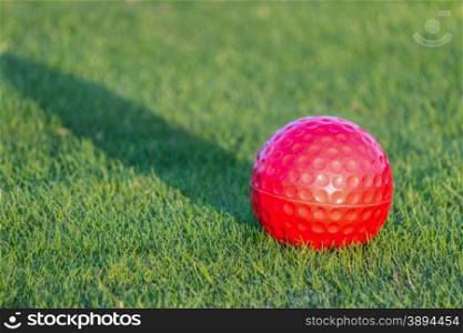 Red golf ball on grass with shadow of evening sun