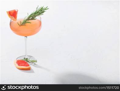 Red grapefruit cocktail in modern luxury martini glass with rosemary and fruit slice on white background. Space for text