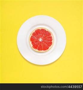 Red grapefruit slice on white plate on yellow background.