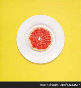 Red grapefruit slice on white plate on yellow background.
