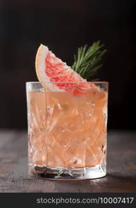 Red grapefruit summer juice cocktail in glass with rosemary and fruit slice on black table background