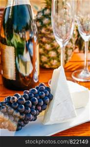 Red grapes and chunk pieces of Brie cheese with champagne bottle and glass in background