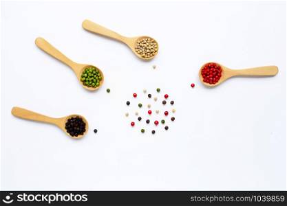 Red, green, white and black peppercorns with wooden spoon on white background.