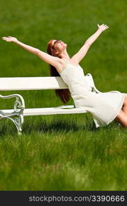 Red hair woman enjoying sun on white bench in a meadow; shallow DOF