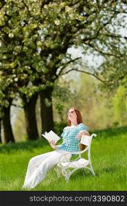 Red hair woman reading book on white bench in a meadow; shallow DOF