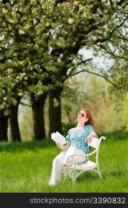 Red hair woman reading book on white bench in a meadow; shallow DOF