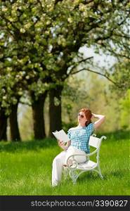 Red hair woman reading white book on a bench in a meadow; shallow DOF
