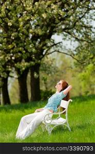 Red hair woman relaxing on white bench in a meadow; shallow DOF