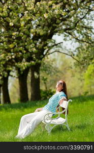 Red hair woman sitting on white bench in a meadow; shallow DOF