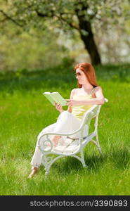 Red hair woman sitting on white bench in a meadow; shallow DOF