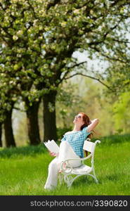 Red hair woman sitting on white bench in green meadow, shallow DOF