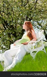 Red hair woman sitting on white bench in green meadow, shallow DOF