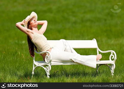 Red hair woman with hat enjoying sun on white bench in green meadow, shallow DOF