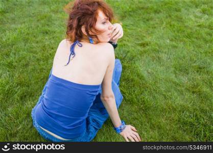 red haired female sitting on fresh grass, back view