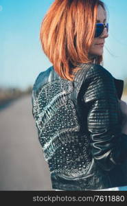 red-haired girl in a black jacket and blue glasses on a gray road