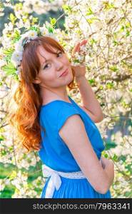 red-haired girl in a blue dress near blossoming cherry in spring