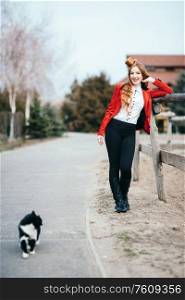 red-haired jockey girl in a red cardigan and black high boots with a cat for a walk