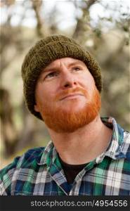 Red haired man with blue plaid shirt looking up in the forest