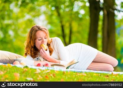 Red-haired student eats an apple and reading books in the park