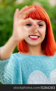 Red haired woman saying Ok with his hand in a park. Focus on the girl