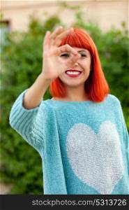 Red haired woman saying Ok with his hand in a park. Focus on the girl