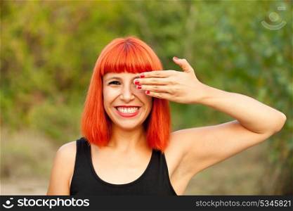 Red haired woman with red nails covering her eyes in a park