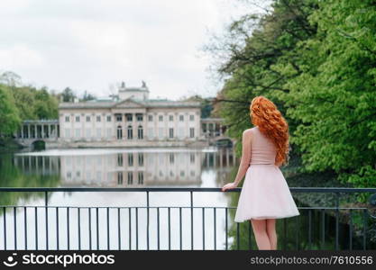 red-haired young girl walking in a park between trees and architectural objects